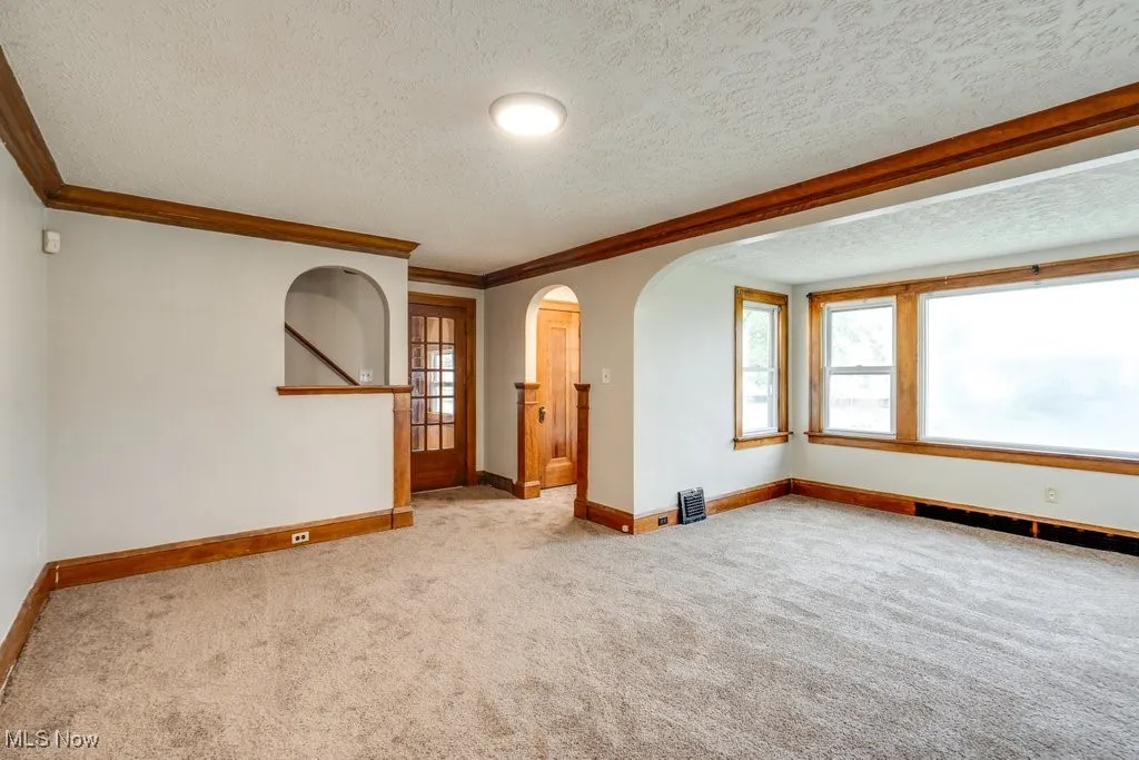 Carpeted empty room featuring arched walkways, a textured ceiling, baseboards, and ornamental molding