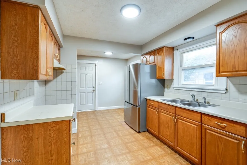 Kitchen with a sink, freestanding refrigerator, light countertops, brown cabinetry, and a textured ceiling