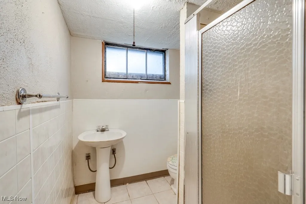 Bathroom featuring toilet, a shower stall, tile patterned floors, a textured ceiling, and wainscoting