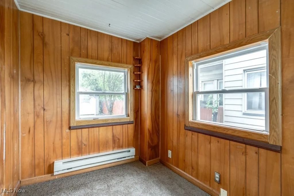 Unfurnished room with baseboard heating, wood walls, carpet flooring, and baseboards