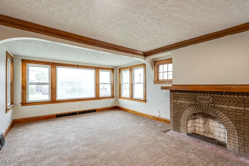 Unfurnished living room with carpet floors, baseboards, arched walkways, a textured ceiling, and ornamental molding