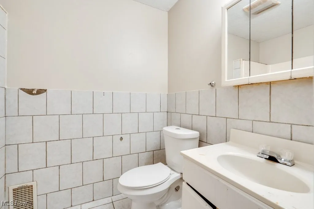 Half bath with tile walls, toilet, and vanity