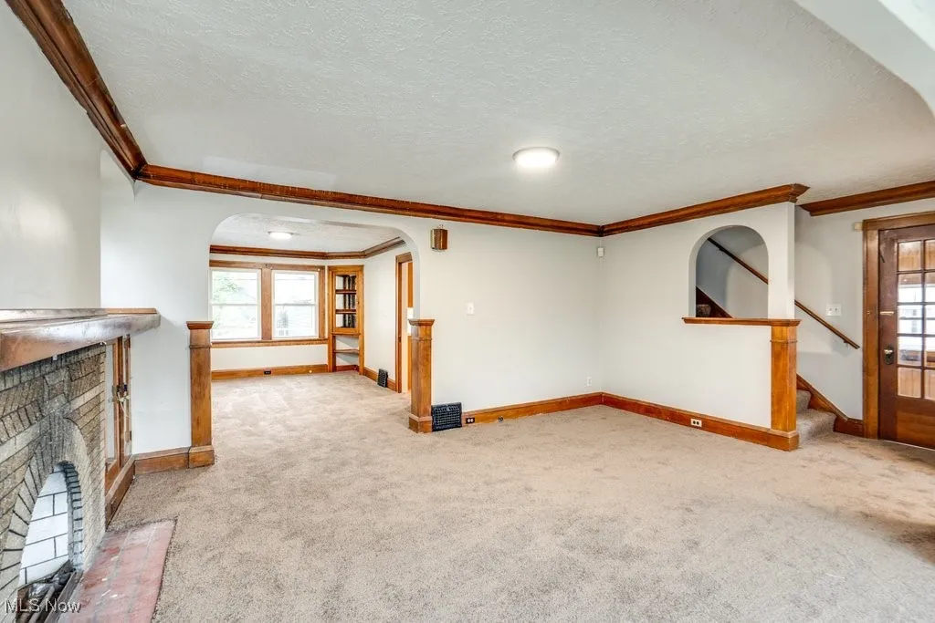 Unfurnished living room featuring arched walkways, carpet floors, a brick fireplace, crown molding, and baseboards