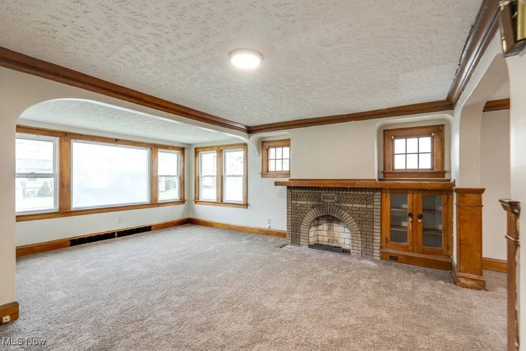Unfurnished living room with a textured ceiling, crown molding, baseboards, carpet flooring, and a​​‌​​​​‌​​‌‌​‌‌​​​‌‌​‌​‌​‌​​​‌​​ fireplace