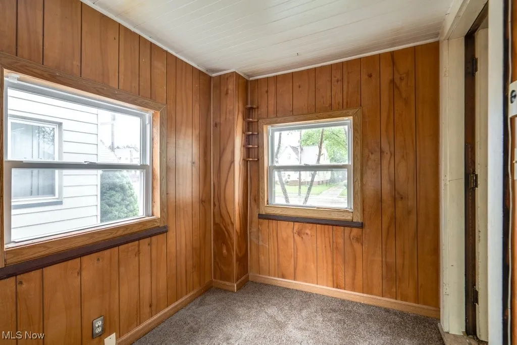 Empty room featuring light colored carpet, wooden walls, and baseboards
