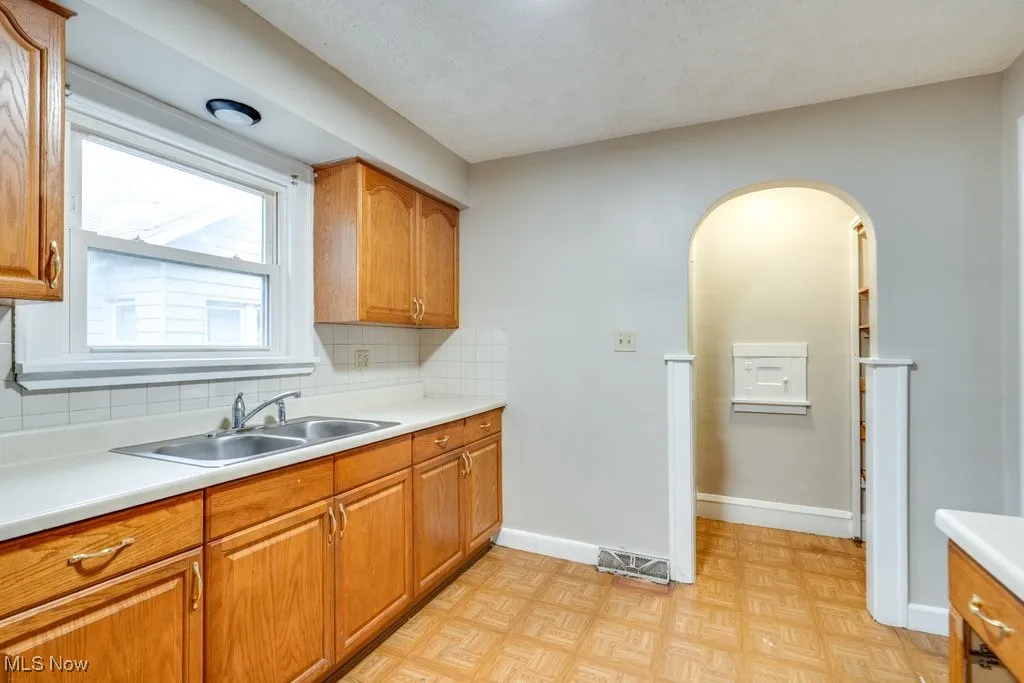 Kitchen with a sink, decorative backsplash, light countertops, brown cabinets, and arched walkways