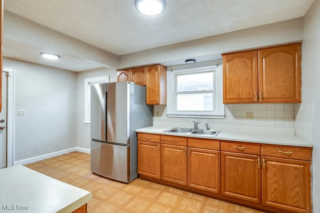 Kitchen with a sink, freestanding refrigerator, brown cabinetry, light countertops, and tasteful backsplash
