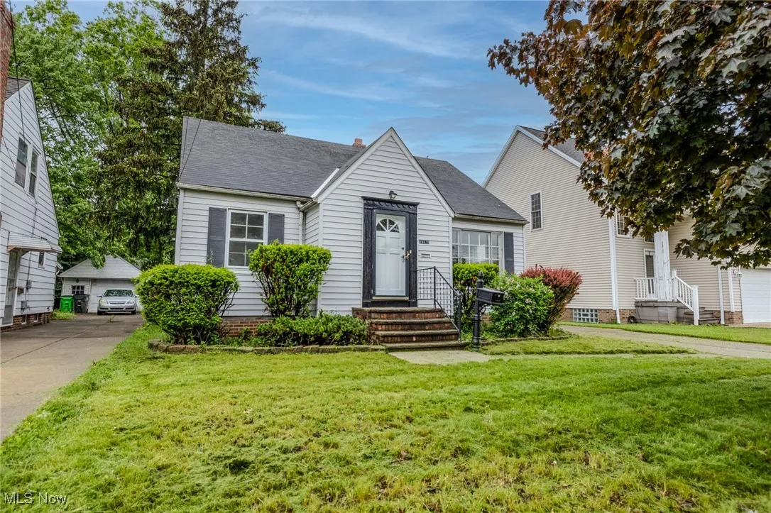View of front of home featuring a front lawn, a shingled roof, a chimney, and a detached garage