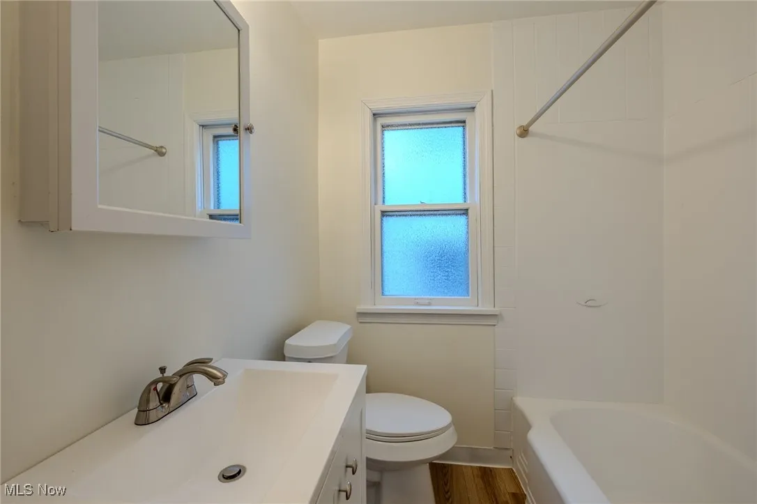 Bathroom with toilet, vanity,  shower combination, and wood finished floors