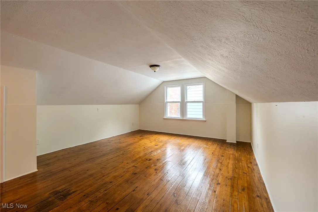 Bonus room featuring hardwood / wood-style floors, lofted ceiling, and a textured ceiling