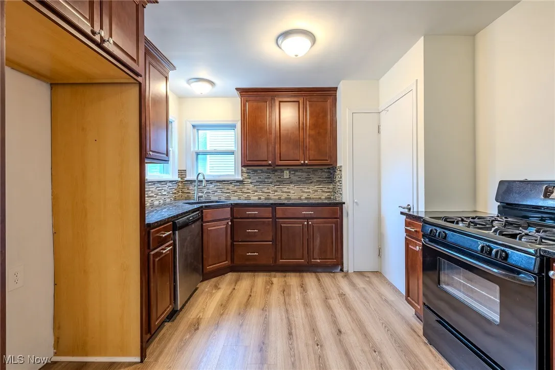 Kitchen with gas stove, dishwasher, light wood-style floors, tasteful backsplash, and a sink