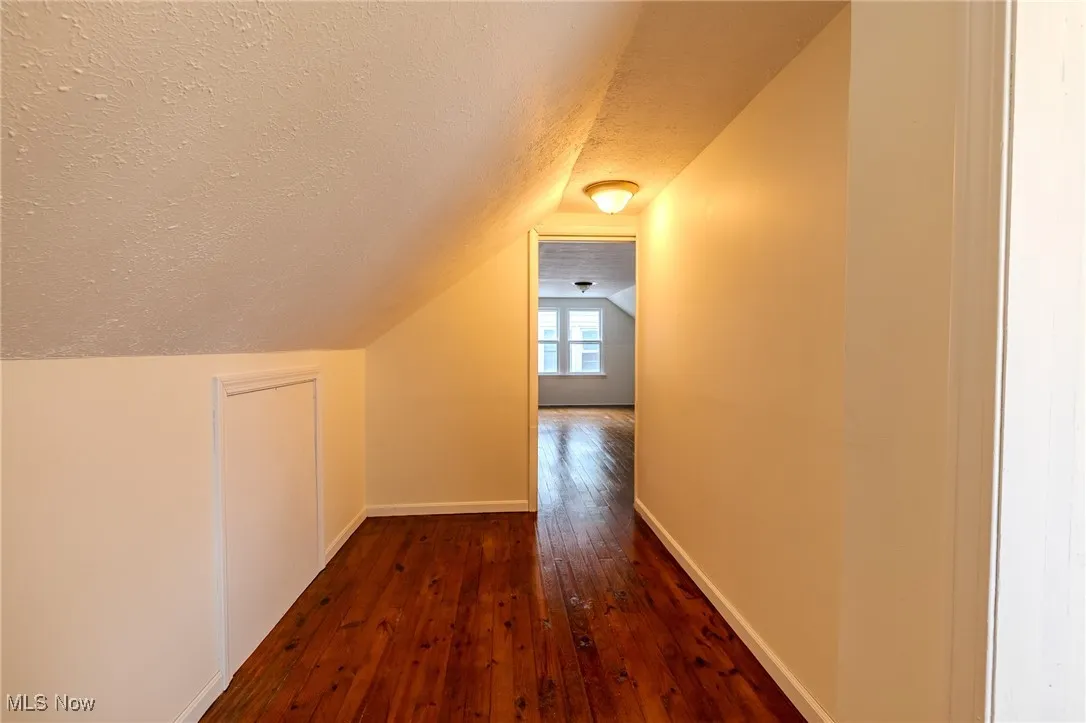 Additional living space with a textured ceiling, hardwood / wood-style flooring, vaulted ceiling, and baseboards