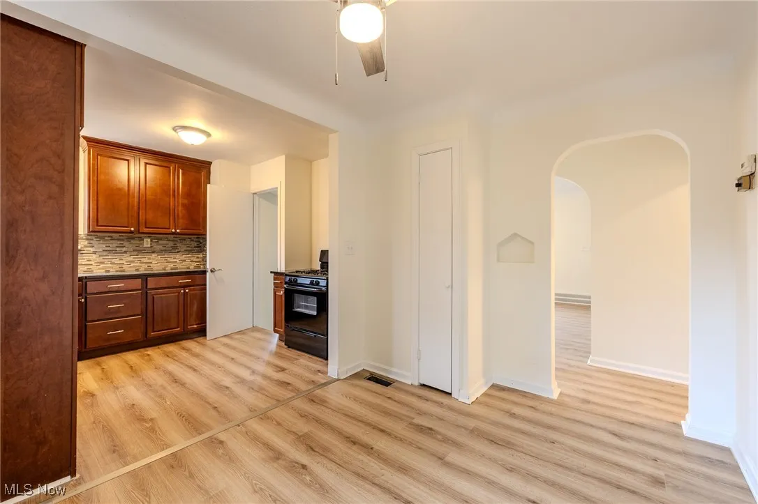 Kitchen featuring black gas range oven, arched walkways, light wood finished floors, dark countertops, and ceiling fan