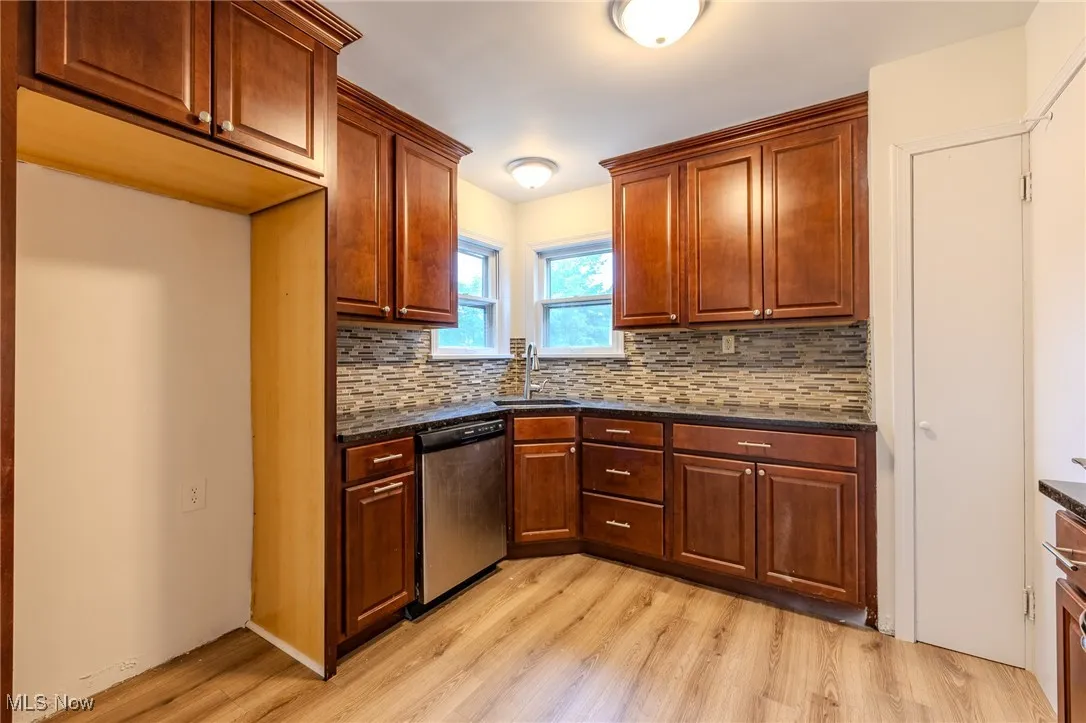 Kitchen with stainless steel dishwasher, a sink, light wood-style flooring, and decorative backsplash