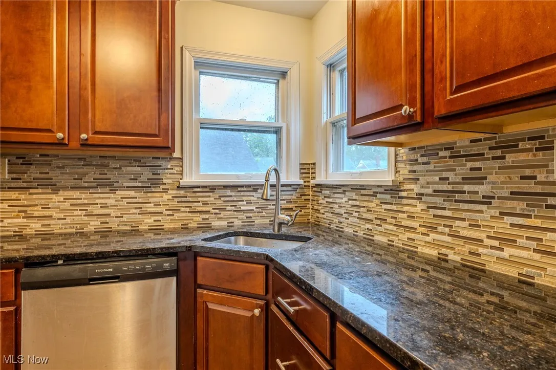 Kitchen with stainless steel dishwasher, a sink, tasteful backsplash, and dark stone counters