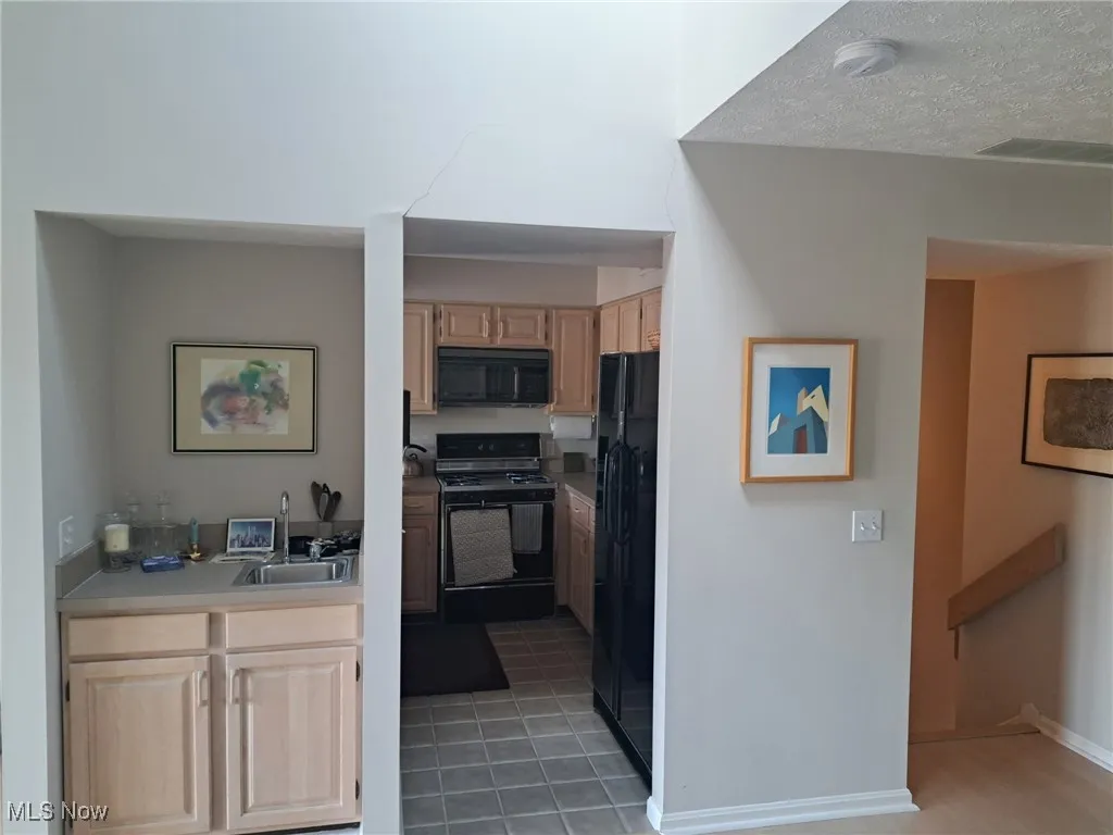 Kitchen featuring black appliances, light brown cabinetry, light countertops, a sink, and baseboards