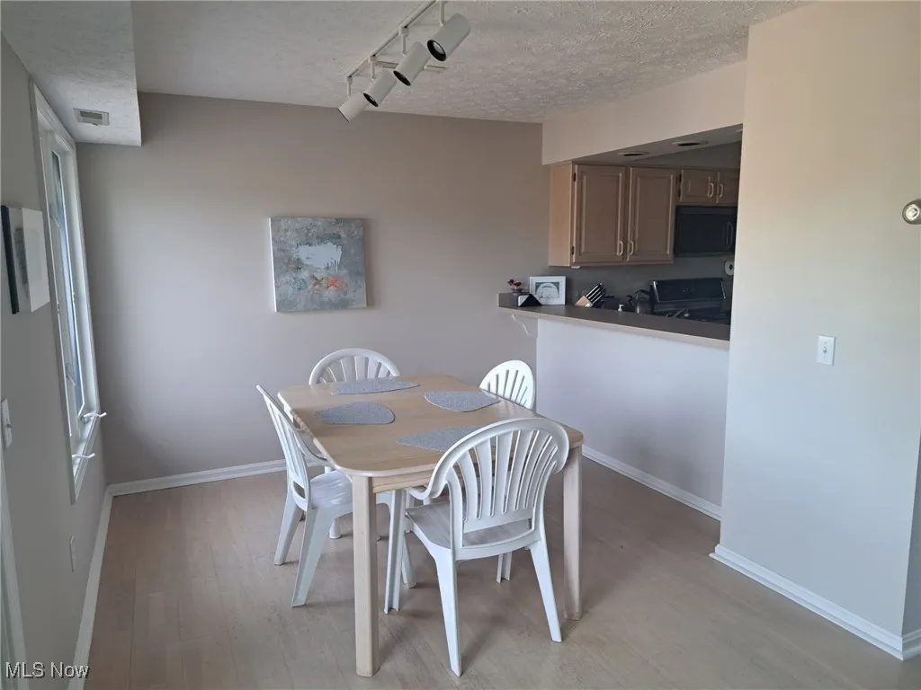 Dining area with a textured ceiling, light wood-style flooring, and baseboards