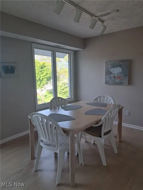Dining space with rail lighting, light wood finished floors, baseboards, and a textured ceiling