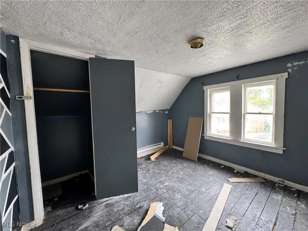 Additional living space featuring baseboard heating, a textured ceiling, lofted ceiling, and baseboards