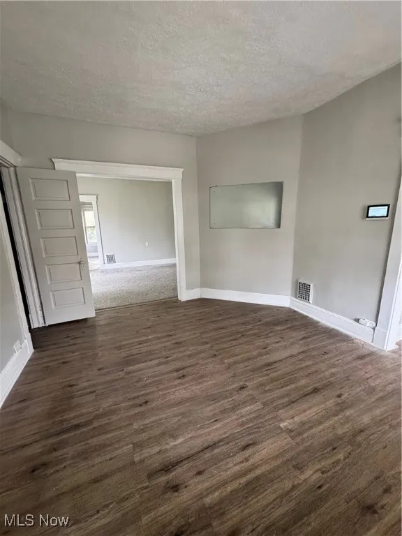 Empty room featuring dark wood-style flooring, a textured ceiling, and baseboards