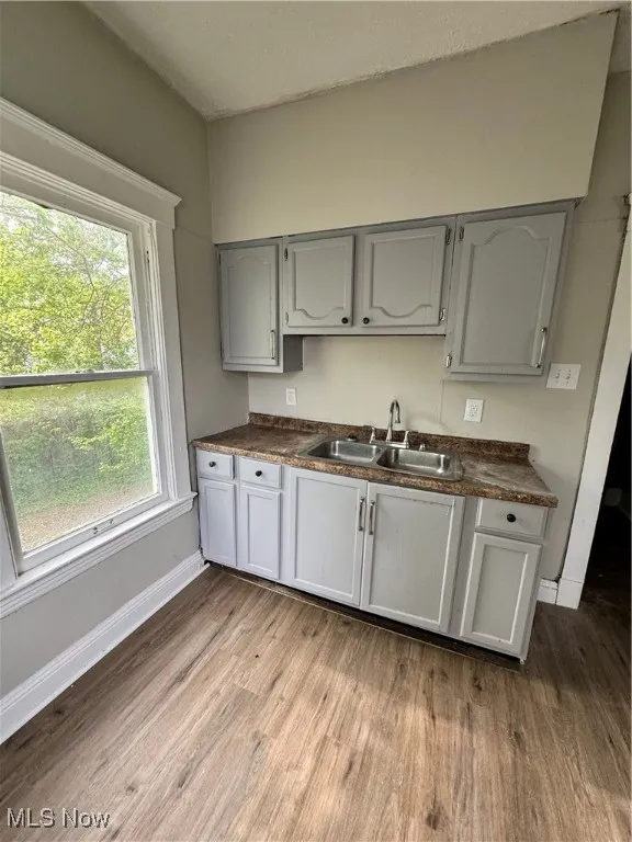 Kitchen with a sink, dark wood-type flooring, dark countertops, and baseboards