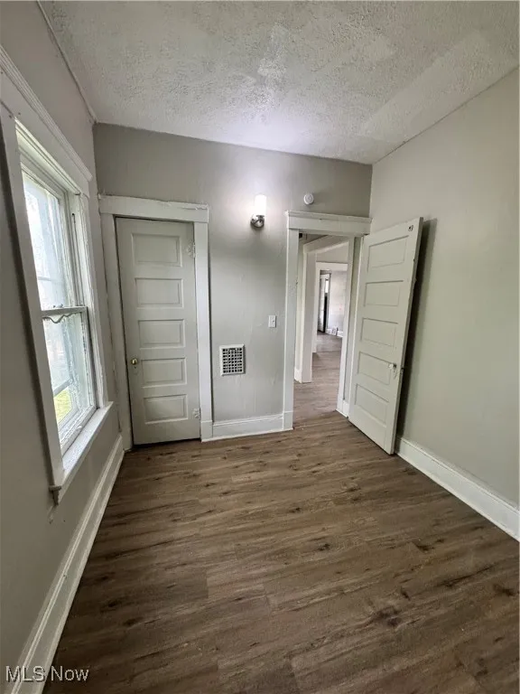 Spare room featuring a textured ceiling, dark wood-style floors, and baseboards
