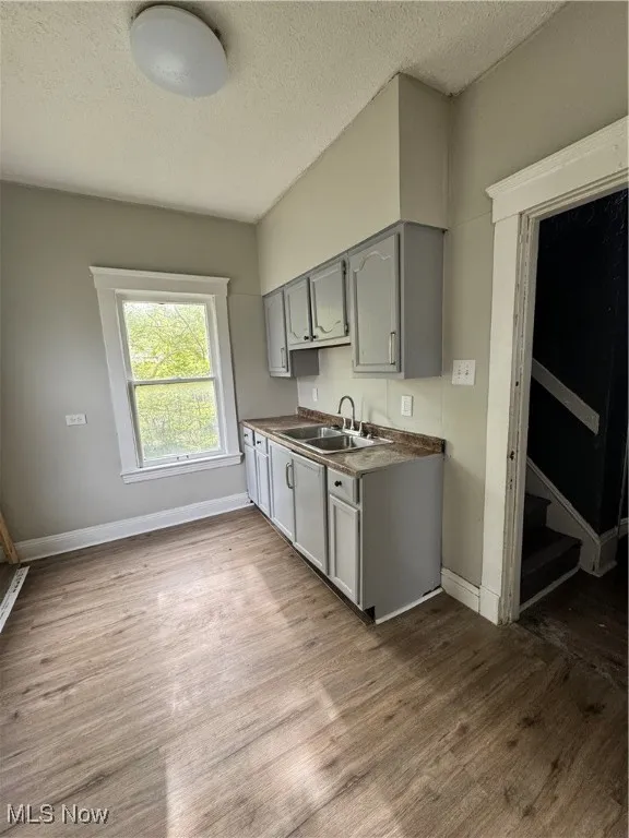 Kitchen featuring gray cabinets, a sink, dark wood-style flooring, a textured ceiling, and baseboards