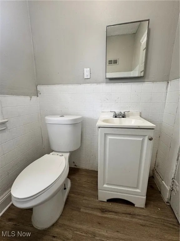 Bathroom with tile walls, wood finished floors, toilet, vanity, and wainscoting