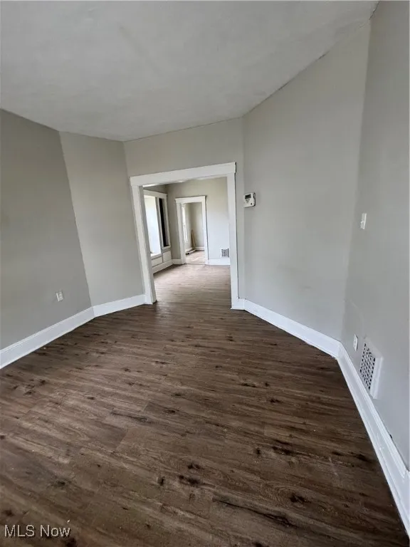 Spare room featuring dark wood-style flooring and baseboards