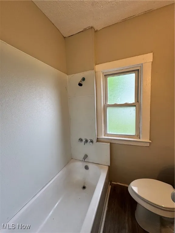 Full bathroom featuring toilet, wood finished floors, a textured ceiling, and  shower combination