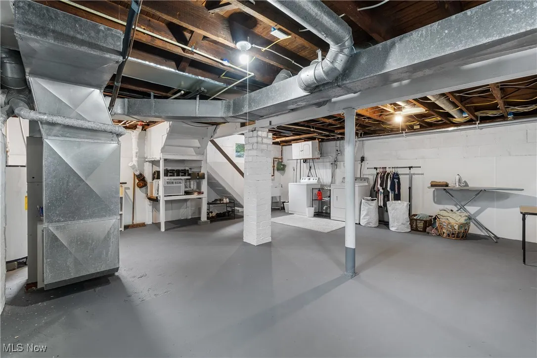 Unfinished basement featuring washer and dryer, stairway, and heating unit