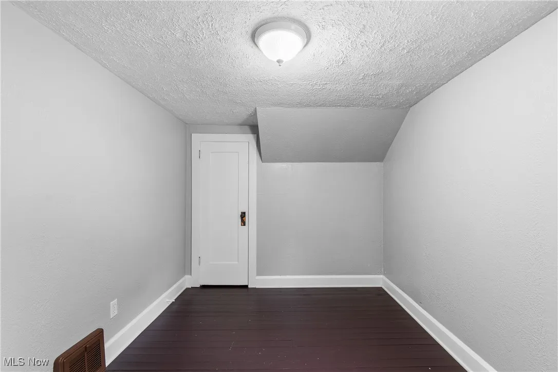 Bonus room with a textured ceiling, dark wood-style floors, and baseboards