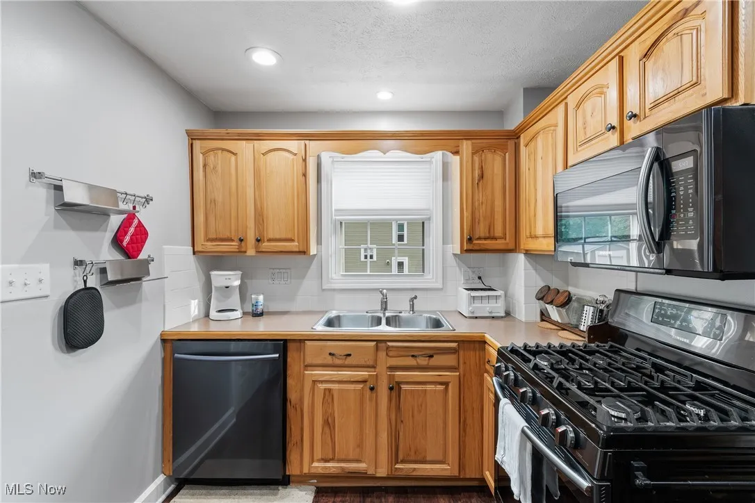 Kitchen featuring gas range, dishwasher, a sink, light countertops, and recessed lighting