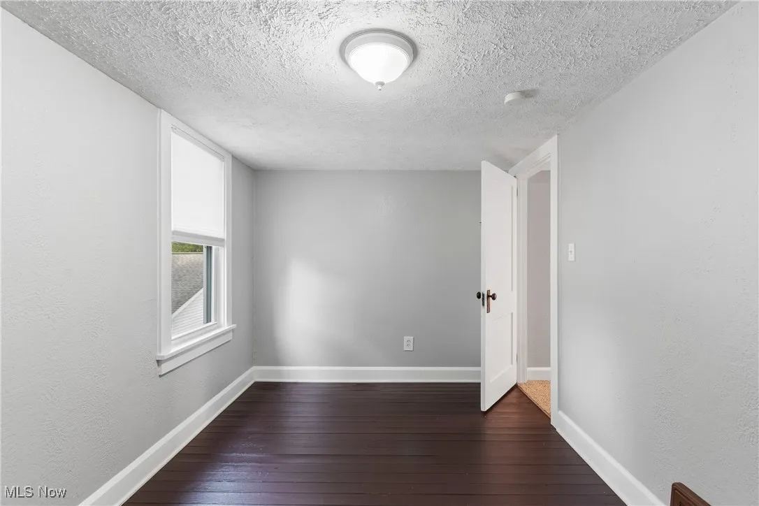 Unfurnished room featuring a textured ceiling, dark wood-style floors, and baseboards