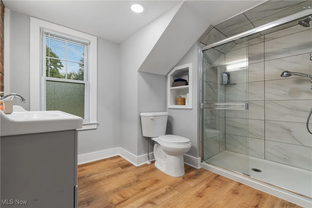 Full bath featuring wood finished floors, toilet, a stall shower, vanity, and lofted ceiling