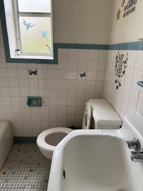 Bathroom featuring tile patterned floors, toilet, and tile walls