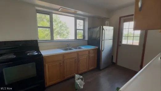 Kitchen with black range with electric stovetop, freestanding refrigerator, light countertops, dark wood-style floors, and brown cabinetry