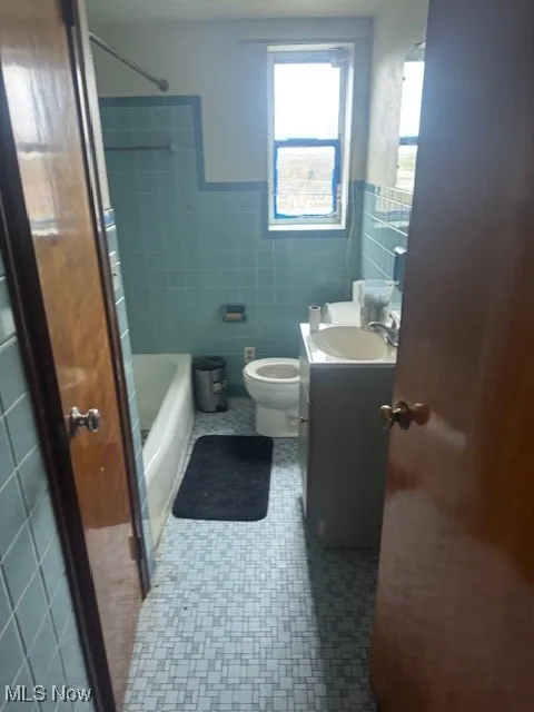 Full bathroom with wainscoting, vanity, shower / bathtub combination, toilet, and tile walls