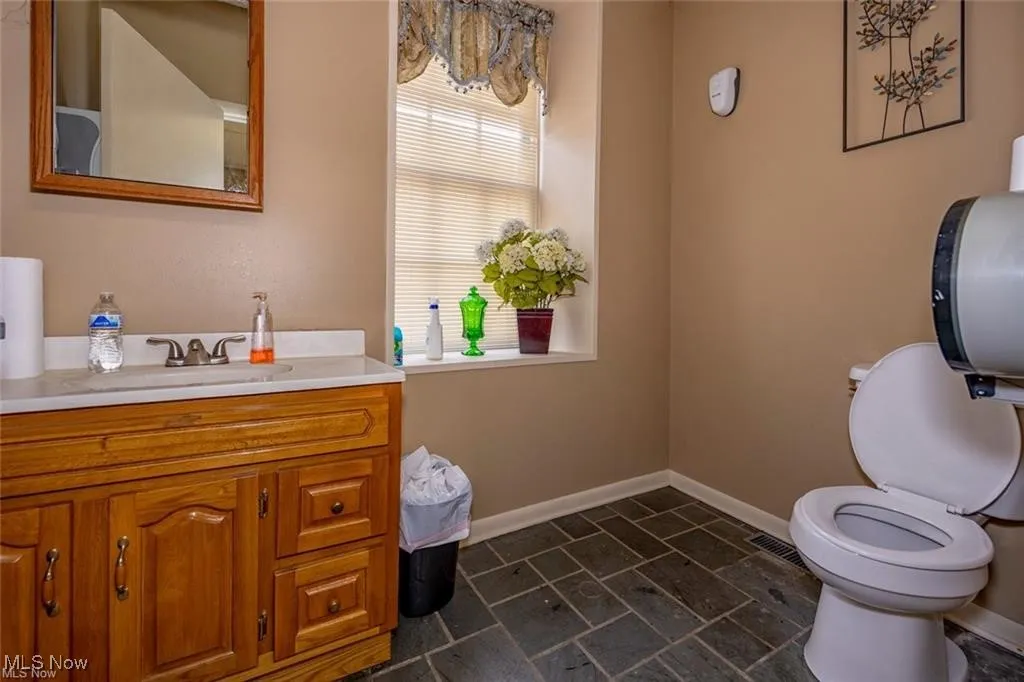 Bathroom with toilet, vanity, baseboards, and stone finish floors