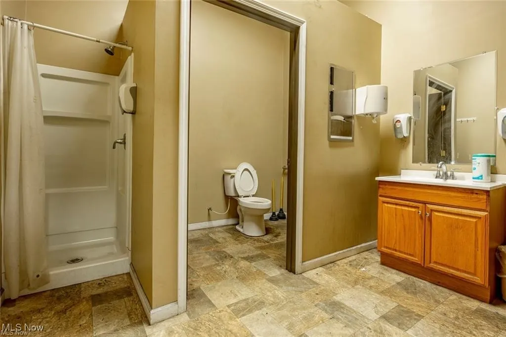 Bathroom featuring vanity, a shower stall, toilet, baseboards, and stone finish floors