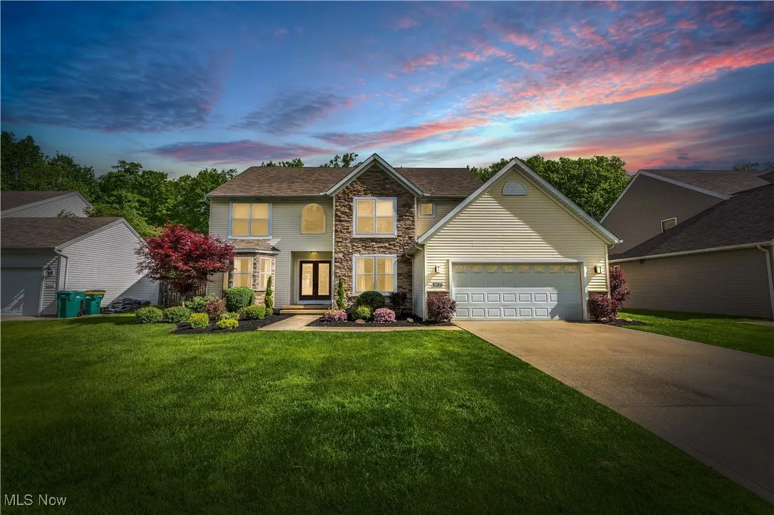 Traditional home with stone siding, driveway, a lawn, and an attached garage