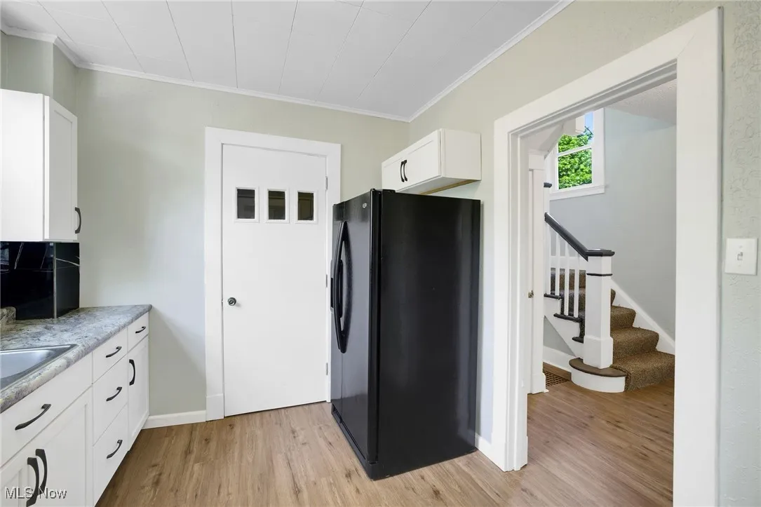 Kitchen with freestanding refrigerator, light wood finished floors, crown molding, white cabinets, and baseboards