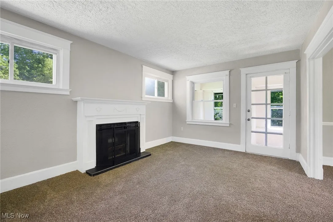 Unfurnished living room with dark carpet, a fireplace with raised hearth, a textured ceiling, and plenty of natural light