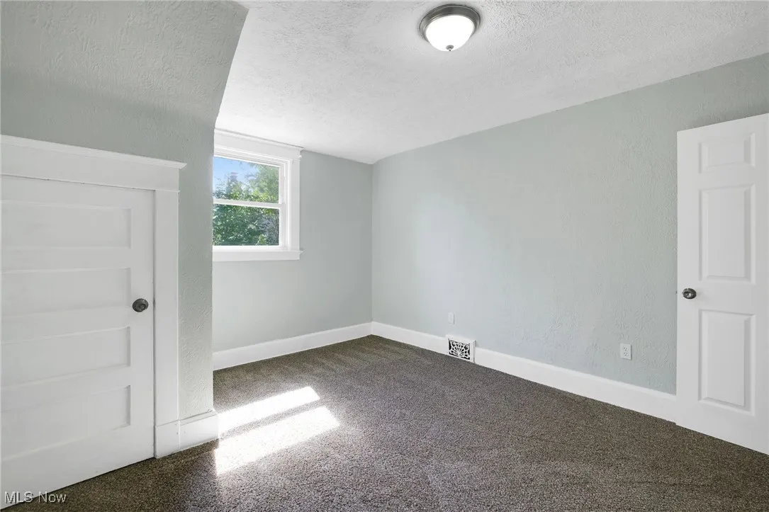Additional living space featuring a textured ceiling, dark colored carpet, and baseboards