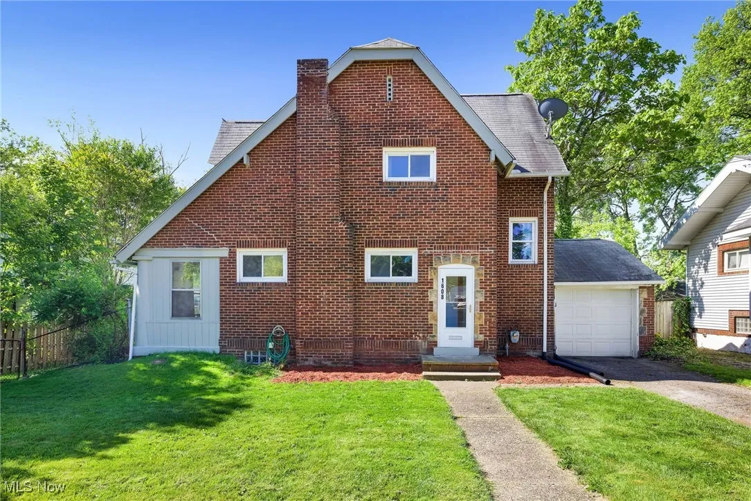 View of front facade featuring asphalt driveway, a chimney, brick siding, a garage, and roof with shingles