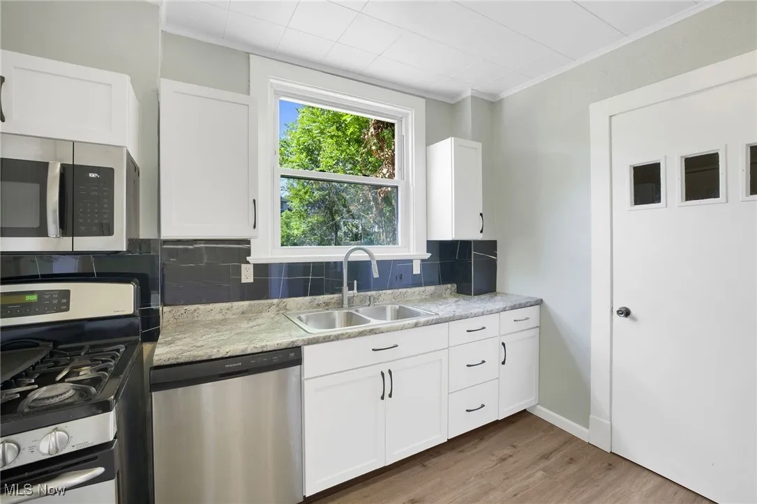 Kitchen featuring appliances with stainless steel finishes, a sink, tasteful backsplash, wood finished floors, and white cabinetry