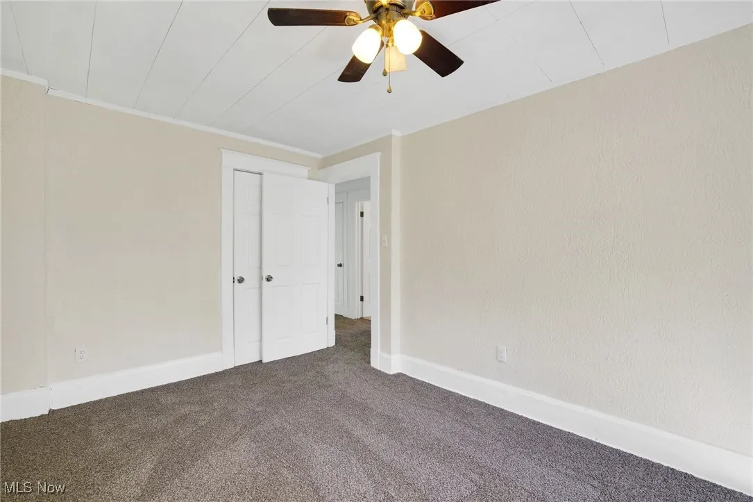 Carpeted empty room featuring ceiling fan, baseboards, and crown molding