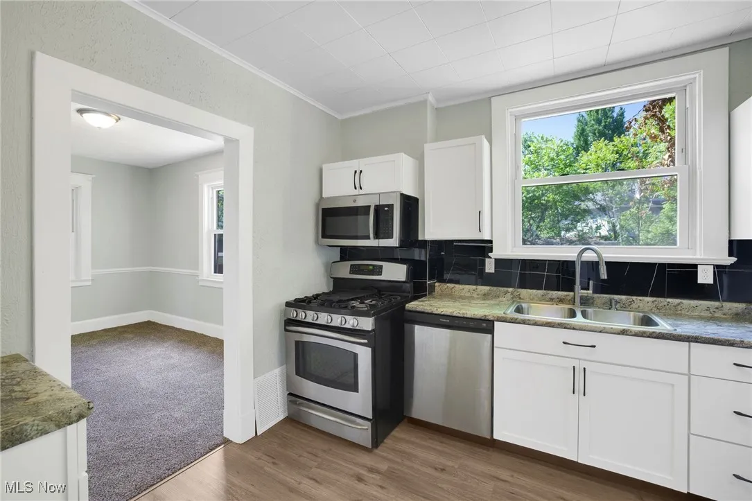 Kitchen with appliances with stainless steel finishes, a sink, white cabinets, crown molding, and backsplash