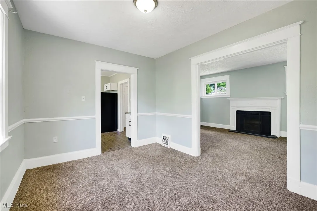 Unfurnished living room with carpet flooring, a fireplace with raised hearth, baseboards, and a textured ceiling