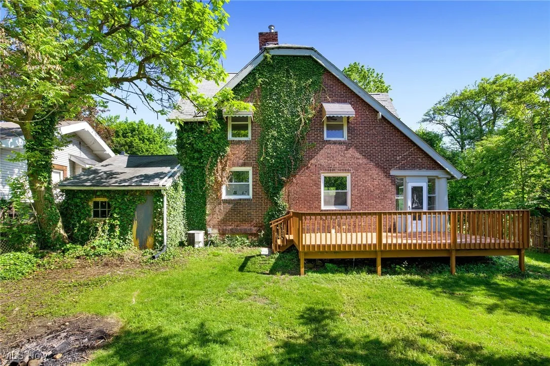 Rear view of property featuring a chimney, brick siding, a yard, a wooden deck, and cooling unit